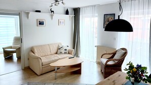 A living room with a beige sofa, a wooden coffee table, a wicker chair, and a vase with flowers.