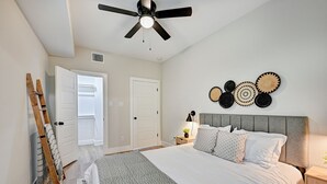 A bedroom with a bed, a ceiling fan, a wall-mounted decorative item, and a bedside table with a lamp. - Central HTX Apt: Free Wi-Fi, A/C, Full Kitchen, Near Top Attractions. (Houston)