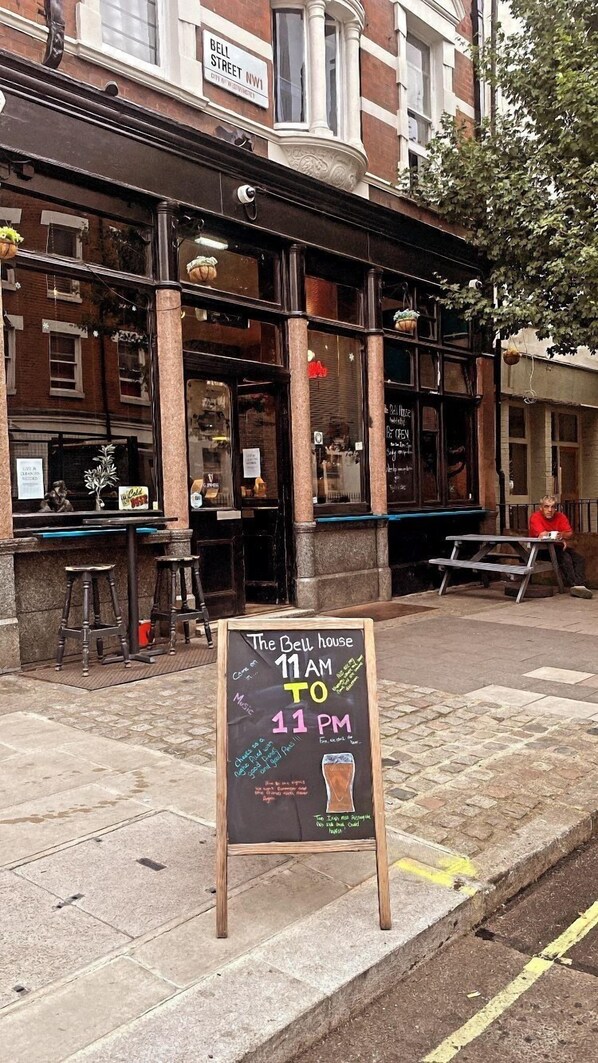 A chalkboard sign outside The Bell House pub, indicating it is open from 11 AM to 11 PM. - Bell House Hostel (London)