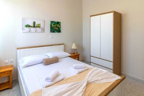 Habitación de hotel con cama, mesita de noche de madera, lámpara, armario y dos adornos en la pared.