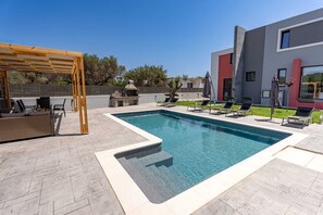Piscina retangular com pergolado de madeira e espreguiçadeiras.