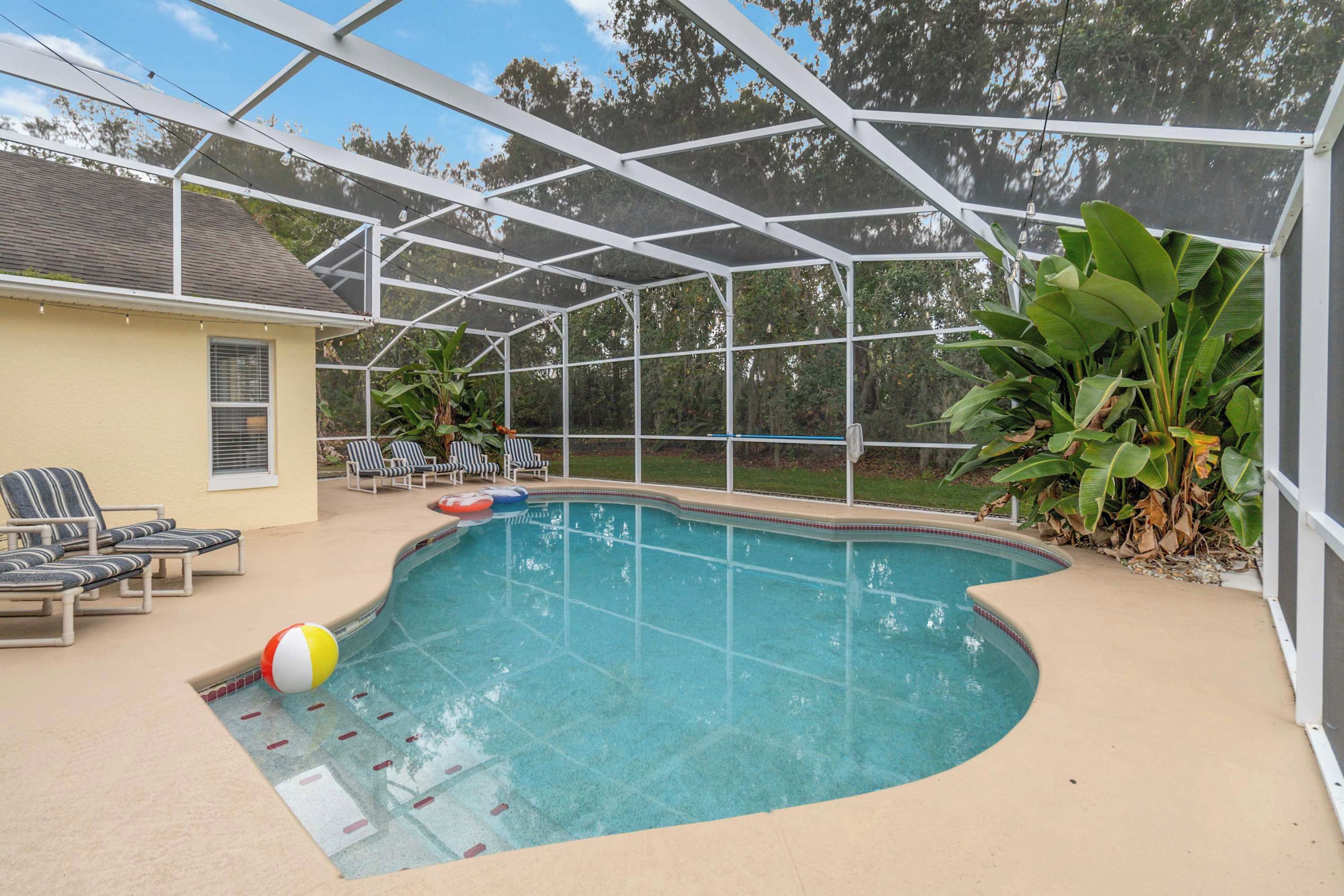 A covered swimming pool with lounge chairs and a beach ball.