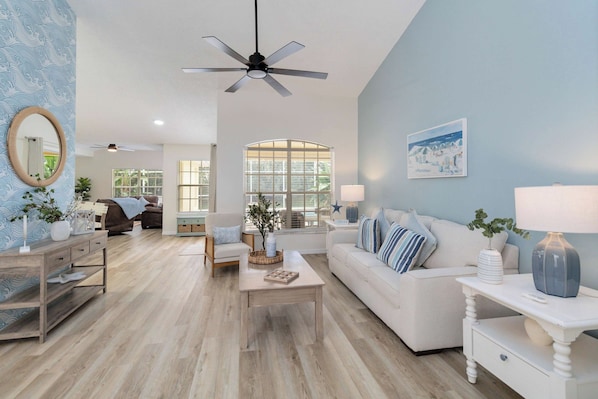 A spacious living room with a ceiling fan, a large window, and a cozy seating area with a sofa and armchairs.