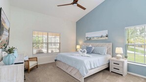 Un dormitorio con cama, mesitas de noche, ventilador de techo y ventanas.