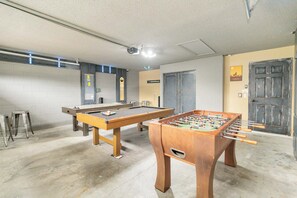 A room with a foosball table, pool table, and two stools.