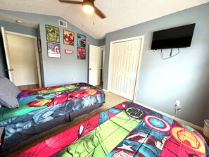 A bedroom with two beds, a ceiling fan, a TV, and multiple superhero-themed wall art.