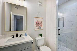 Ein Badezimmer mit einem weißen Waschbecken, schwarzen Wasserhähnen, einer Toilette und einer Dusche mit Glastüren.