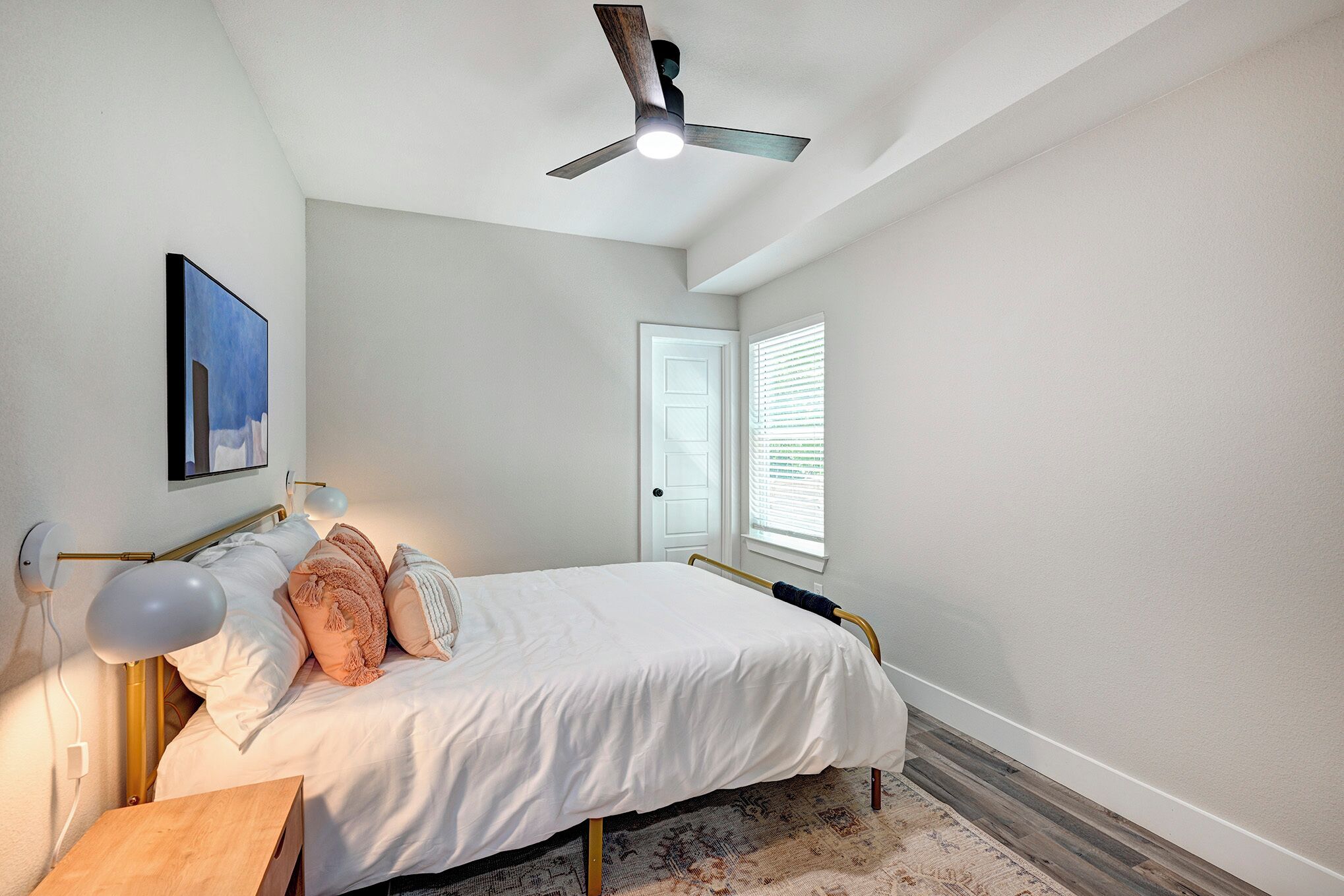 Une chambre à coucher avec un lit, des lampes de chevet, un ventilateur de plafond, une porte et une fenêtre avec des stores.