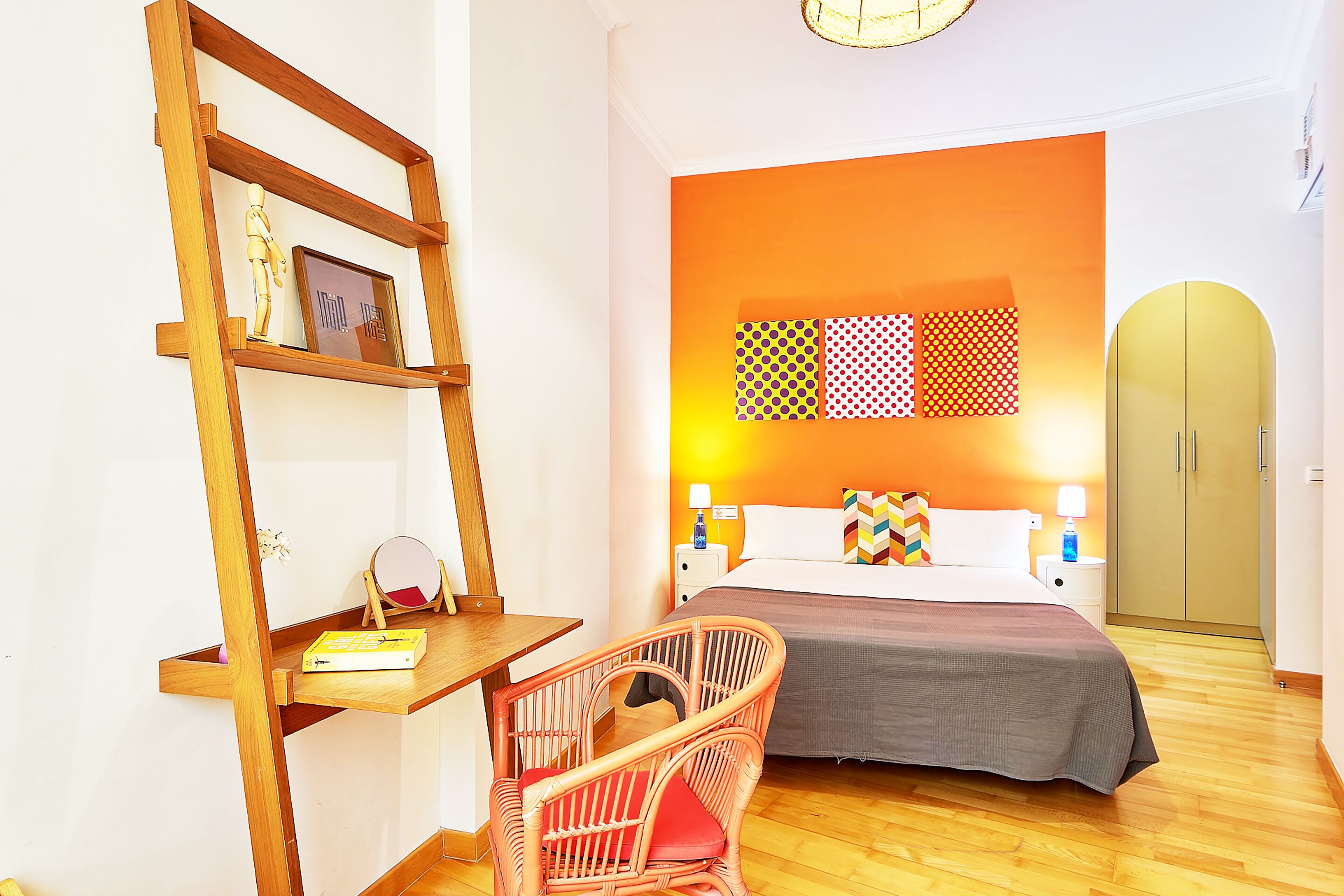 Un dormitorio con escritorio de madera, una silla de mimbre, cama con pared de acento naranja, decoración mural estampada y un armario.