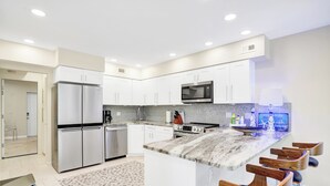 Una cocina moderna con electrodomésticos de acero inoxidable, armarios blancos y encimera de mármol, además de taburetes de bar.