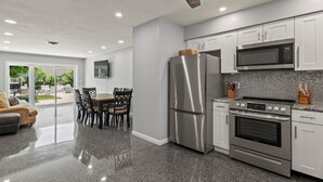 Una cocina moderna con electrodomésticos de acero inoxidable, un comedor con mesa y sillas, y un ventilador de techo.