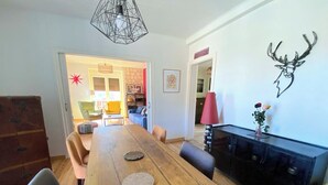 Un coin repas avec une table en bois, des chaises et un buffet noir. On aperçoit une lampe rouge posée sur le buffet et une décoration représentant une tête de cerf au mur.