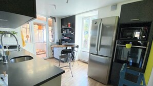 Une cuisine moderne équipée d’un réfrigérateur en acier inoxydable, d’un four encastré et d’un évier. On y trouve également un coin repas avec une chaise et une petite table.