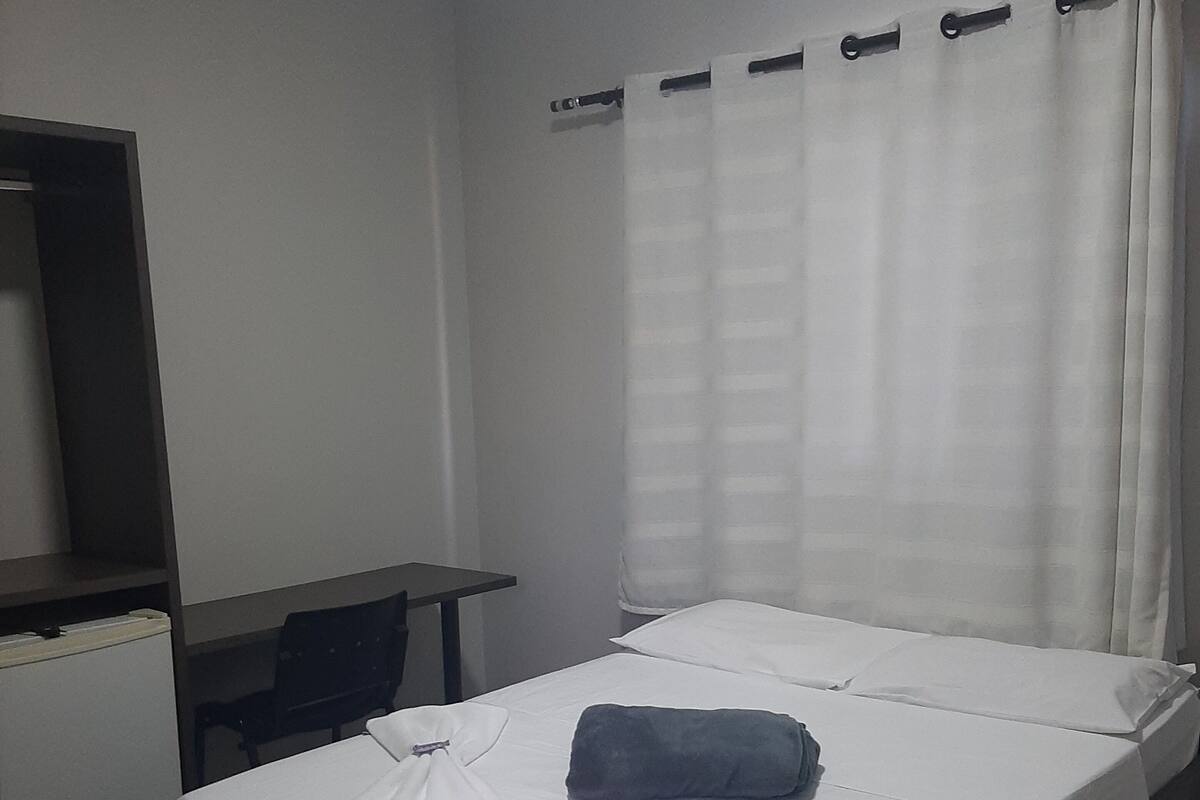 A hotel room with a bed, a desk, a chair, and an air conditioning unit.