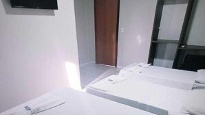 A hotel room with three single beds, a flat-screen TV mounted on the wall, a wooden door, and a mirror.