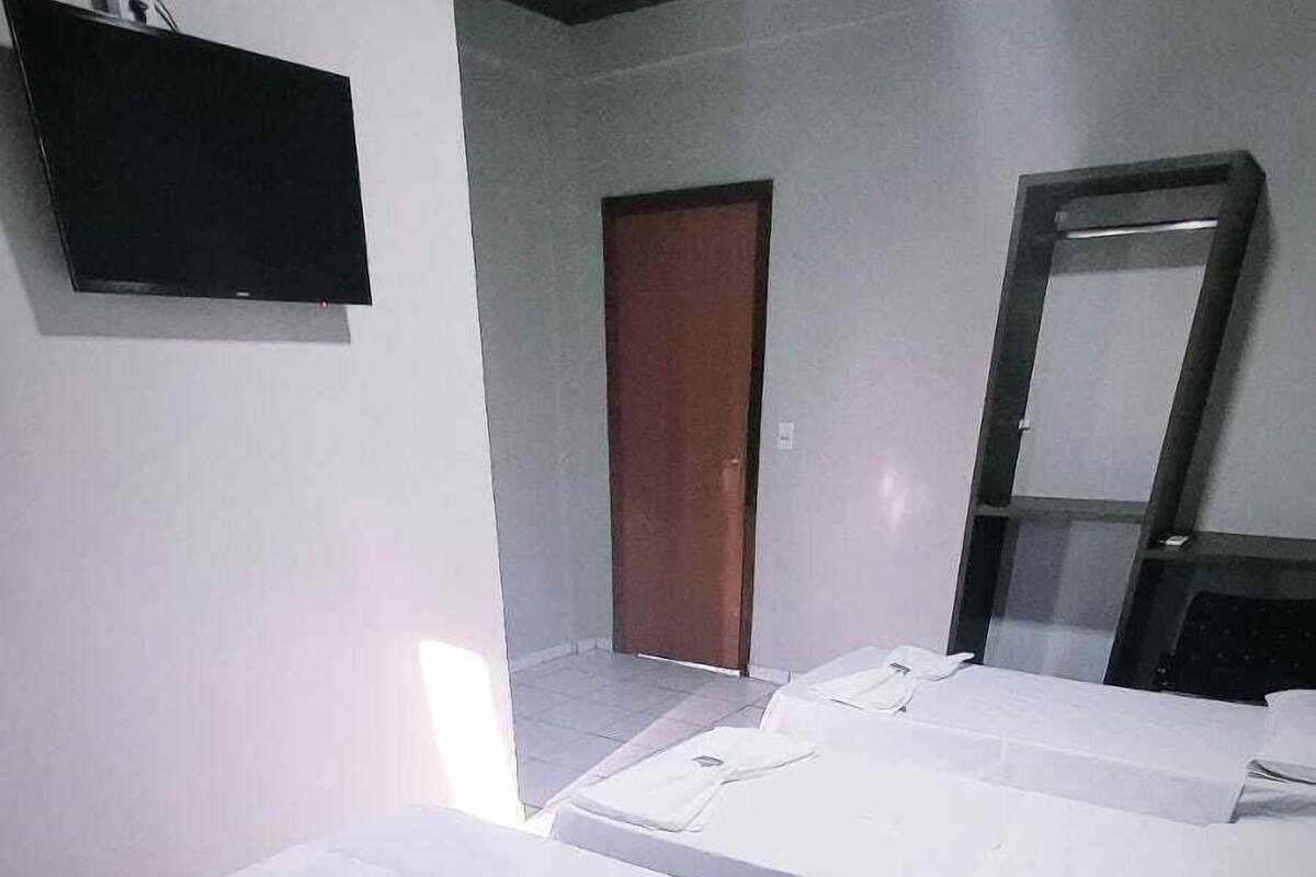 A hotel room with three single beds, a flat-screen TV mounted on the wall, a wooden door, and a mirror.