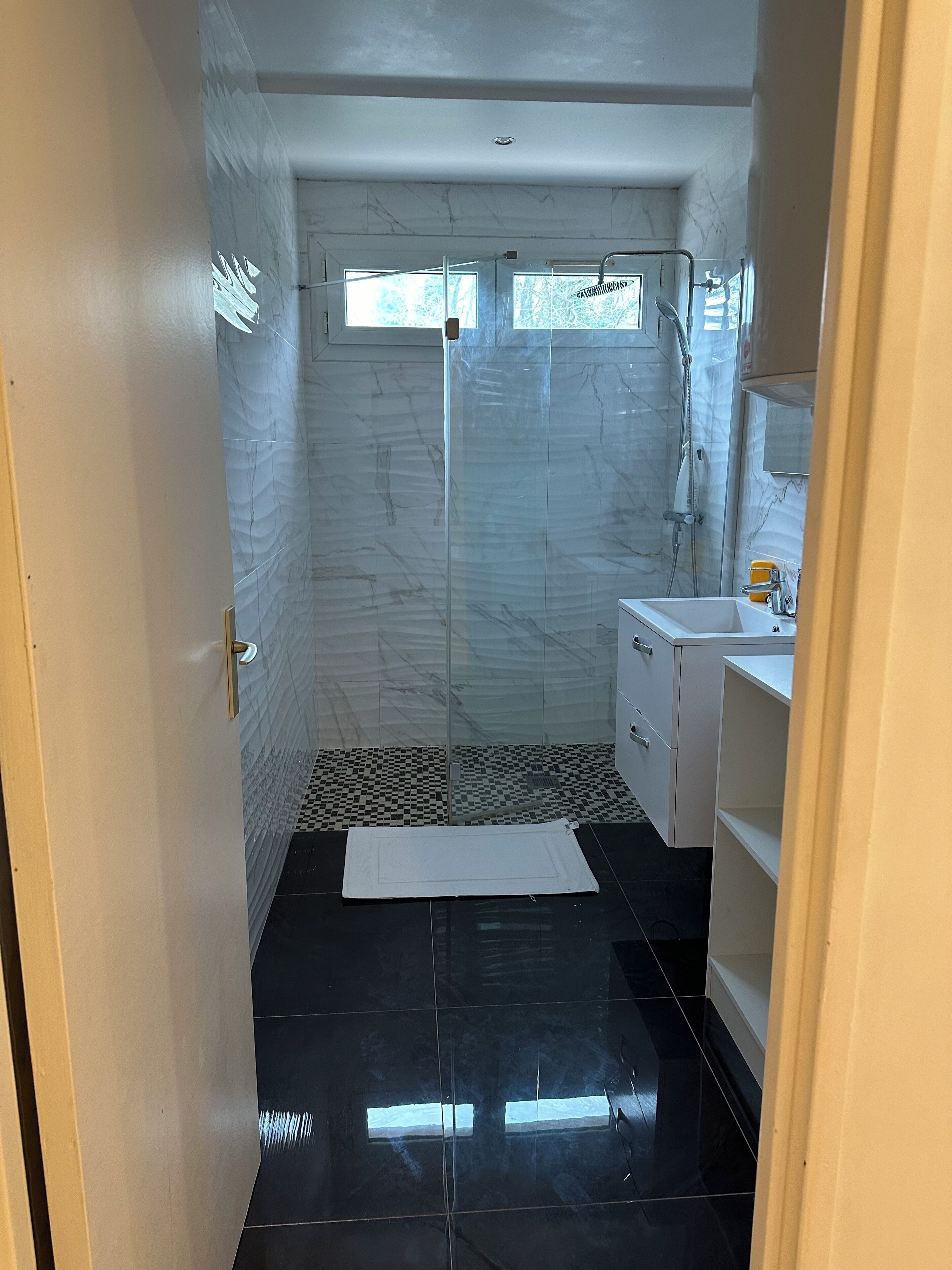Une salle de bain avec une douche à parois de verre, un lavabo blanc et un sol carrelé.
