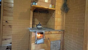 A compact kitchen with a wood-burning stove, a small shelf with kitchenware, and a wicker basket on the floor.