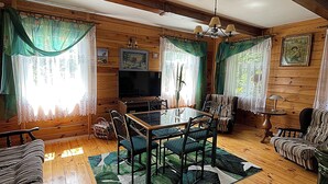A cozy log cabin interior with a dining table, chairs, a sofa, and a television.