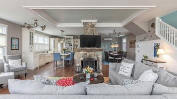 A spacious living room with a stone fireplace, a large grey sofa, and a dining area with a high ceiling.