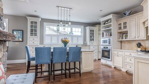 A kitchen with white cabinetry, a dining area with blue chairs, and a large window. - Charming 3-bedroom house steps to Pine Point Beach with backyard oasis (Scarborough)