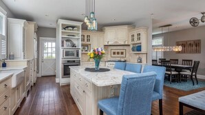 A spacious kitchen with white cabinetry, a marble island, and blue upholstered chairs. - Charming 3-bedroom house steps to Pine Point Beach with backyard oasis (Scarborough)