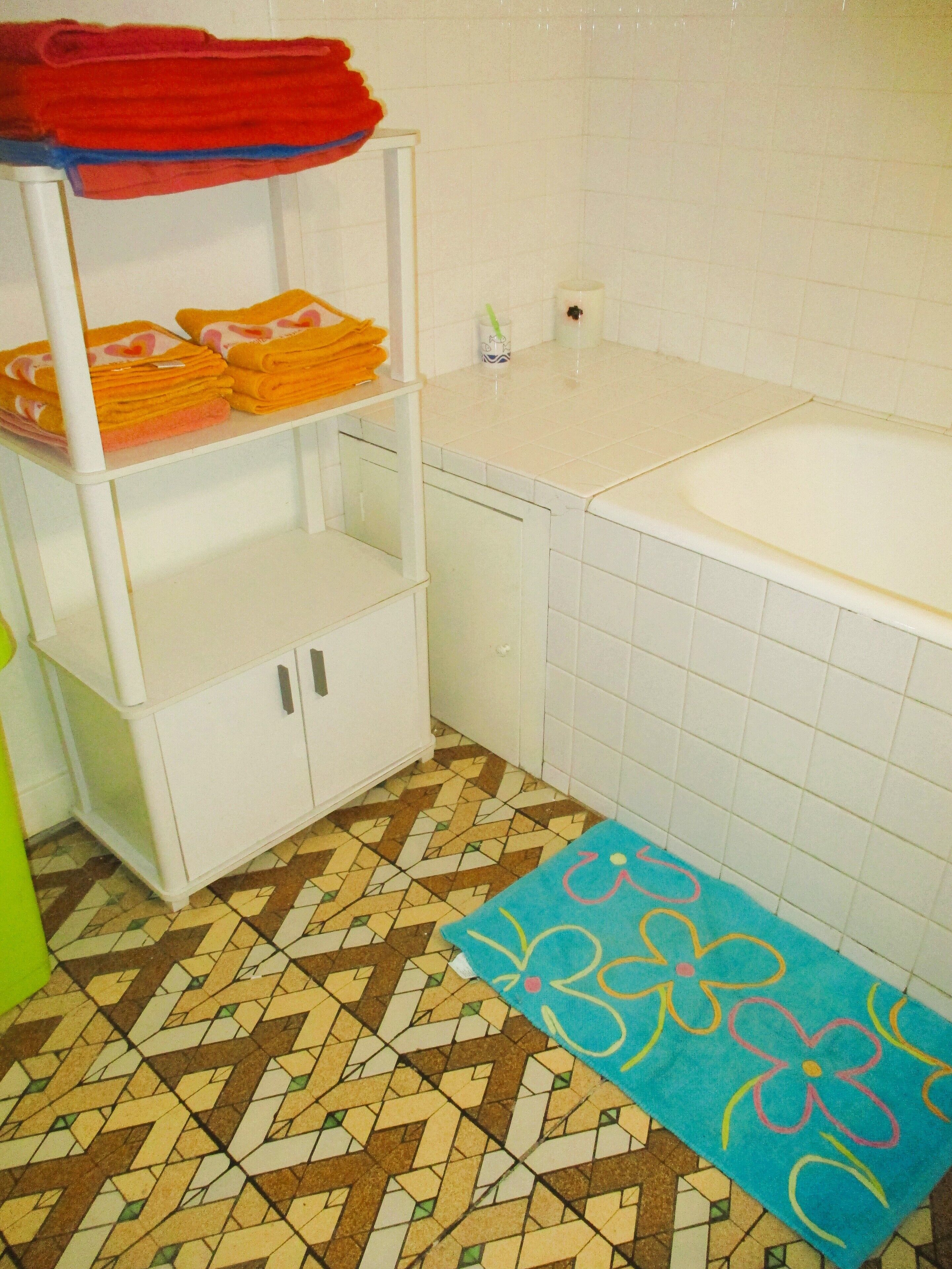 A bathroom with a white sink, a tiled floor, and a shelf with folded towels.