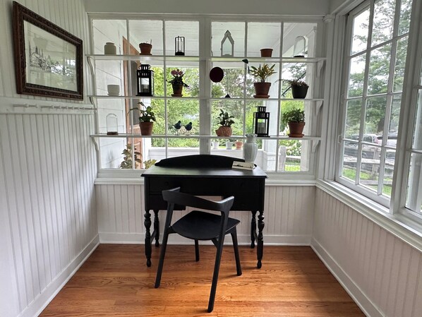 A room with a wooden desk, a chair, a window with a view of greenery, and shelves with potted plants and decorative items. - Private Unit in shared 1830 Farmhouse (Hillsdale)
