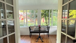Une pièce dotée d’un plancher en bois, d’une table entourée de chaises et de grandes fenêtres aux montures blanches.
