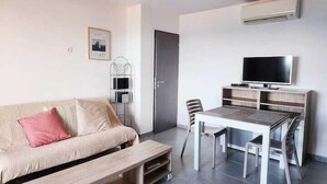 A modern living room with a sofa, a coffee table, a dining table with chairs, a TV, and a built-in air conditioning unit. - Appartement vue mer Entre Collioure et Cadaquès (Cerbère)