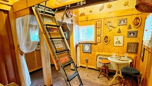 Une cuisine avec un intérieur en bois, une échelle, un évier et une fenêtre avec des rideaux.