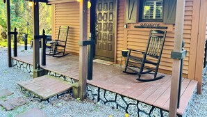 Une cabane en bois avec une véranda, des fauteuils à bascule et une pancarte indiquant « Bienvenue ».
