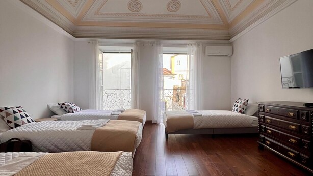 A hotel room with three beds, wooden flooring, a large mirror, and a decorative ceiling.