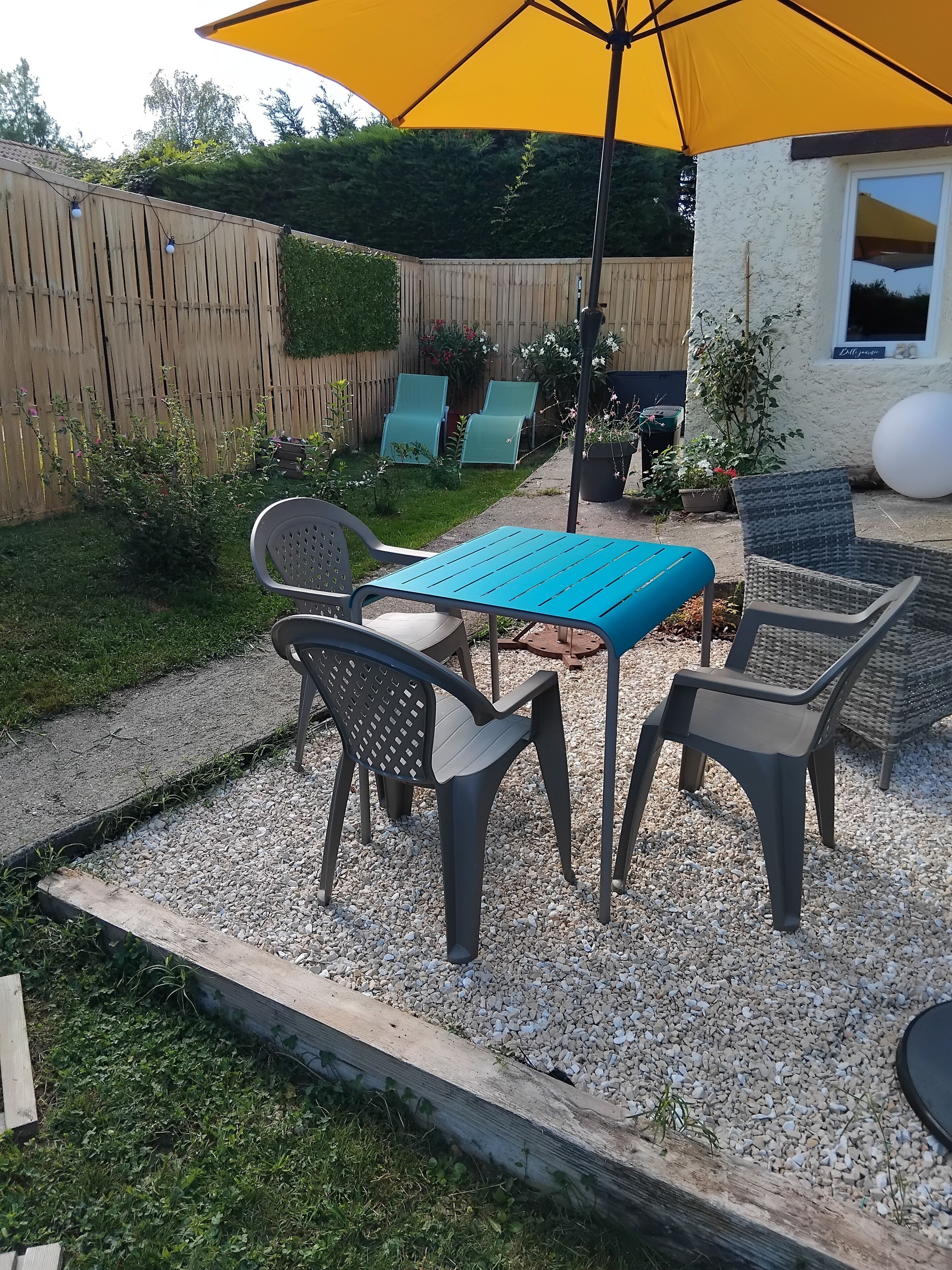 An outdoor patio with a table and chairs, surrounded by a wooden fence and potted plants.