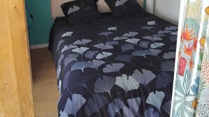Un dormitorio con pared color turquesa, una cama con edredón de estampado floral oscuro y dos obras de arte colgadas en la pared que representan figuras humanas abstractas.