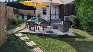 Un patio al aire libre con una mesa, sillas, un paraguas amarillo y un pequeño jardín.