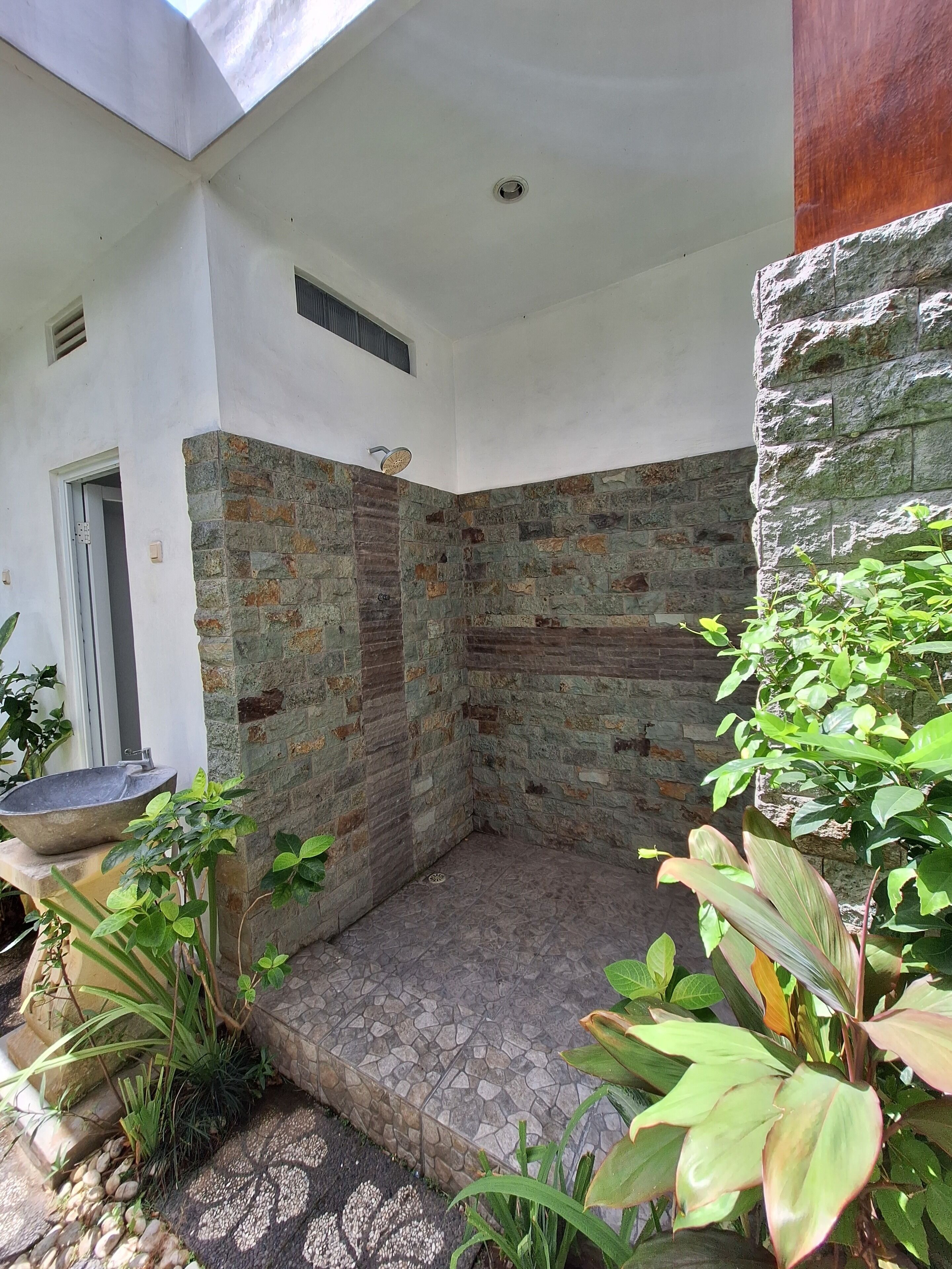 A small, enclosed outdoor area with a stone wall, a tiled floor, and potted plants.