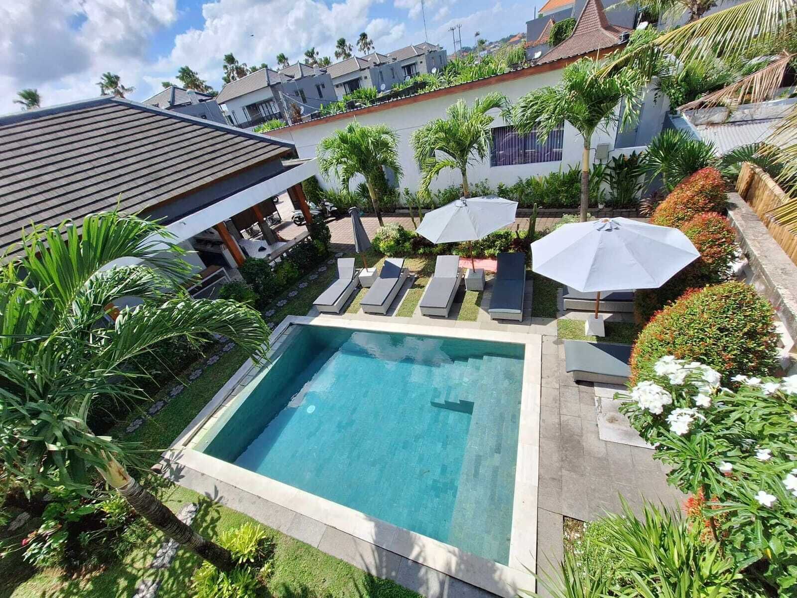 Ein rechteckiger Swimmingpool mit Liegestühlen und Sonnenschirmen, umgeben von üppiger Vegetation und Palmen.