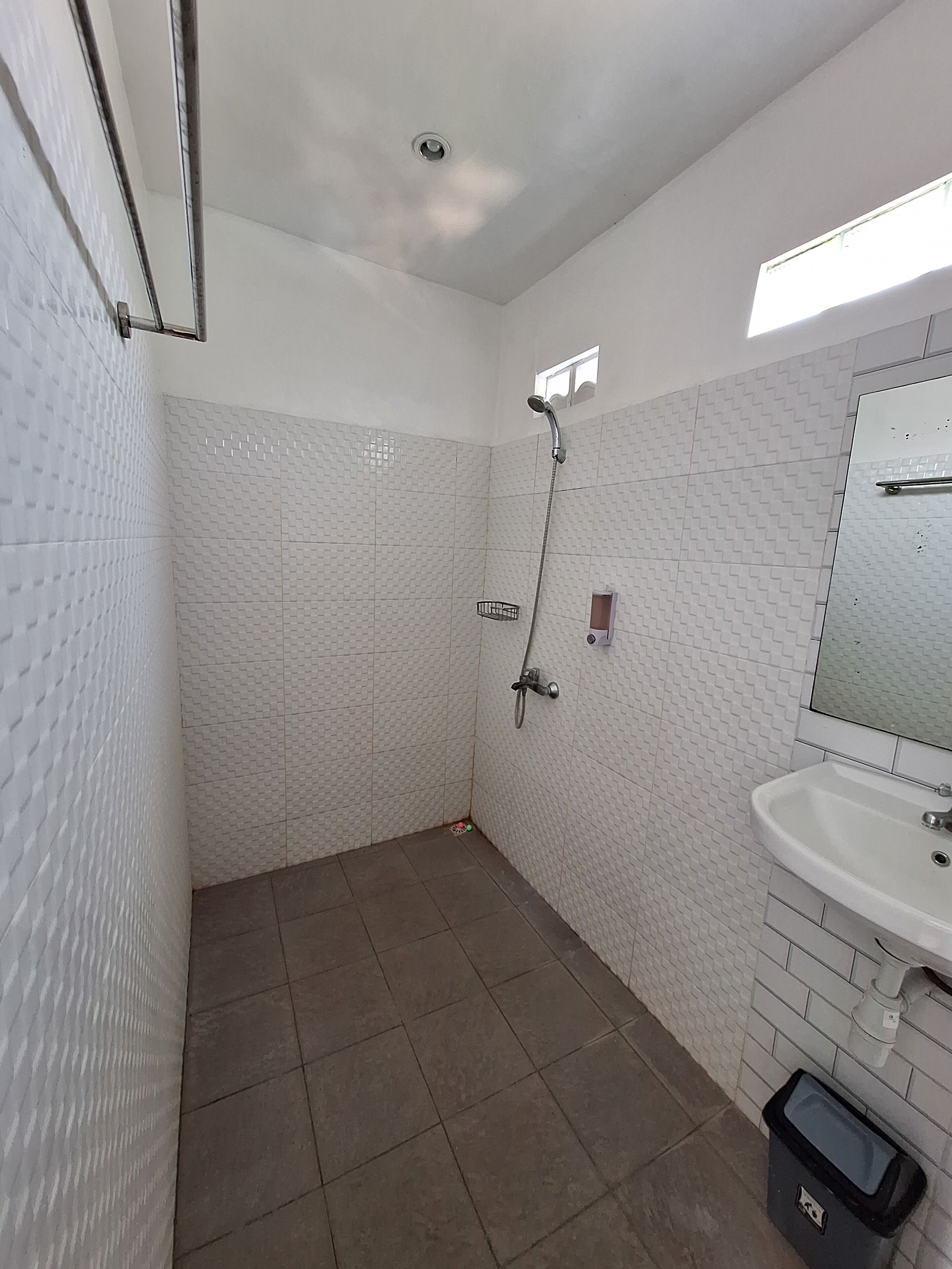 A bathroom with white tiled walls, a shower, a sink, and a trash bin.
