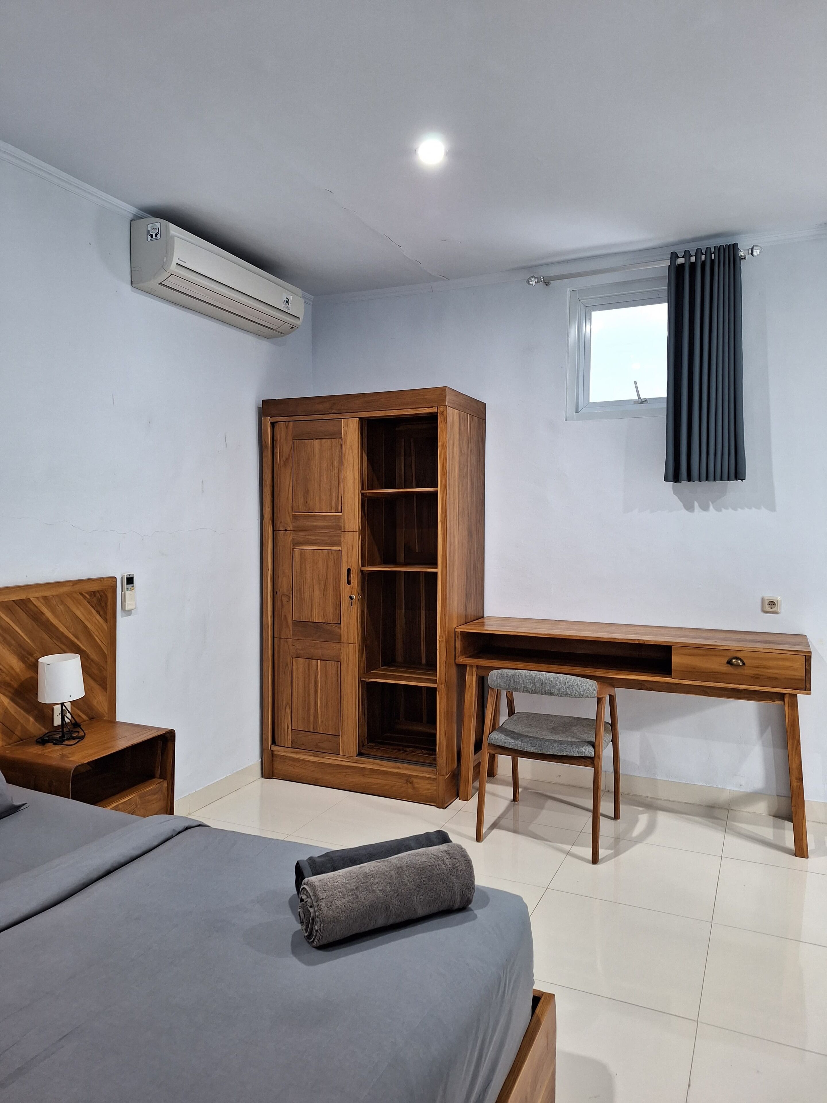 Ein Schlafzimmer mit einem Bett, einem Holzschrank, einem Schreibtisch mit Stuhl und einem Fenster mit Vorhängen.