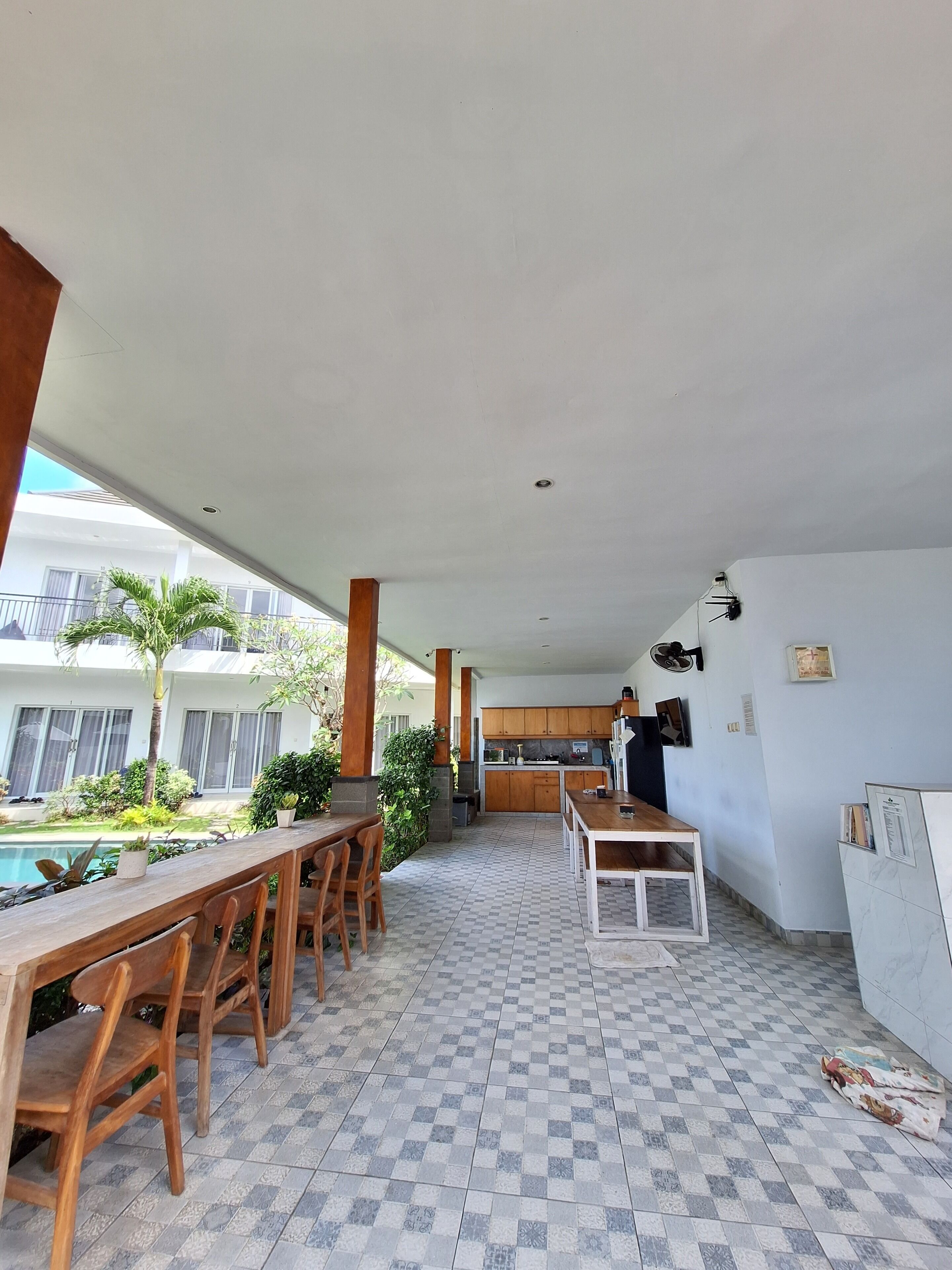 Un área de comedor al aire libre techada con piscina, muebles de madera y una cocina al fondo.