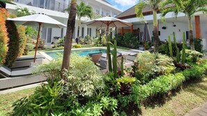A resort with a swimming pool, palm trees, and a white building with balconies. - Bonewood Guesthouse (Canggu)