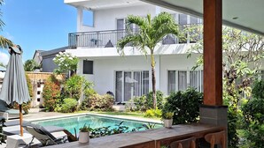 A poolside area with a wooden table and chairs, a pool, and a two-story building in the background. - Bonewood Guesthouse (Canggu)