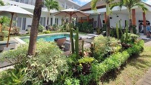 A resort pool area with palm trees, lounge chairs, and a building with balconies. - Bonewood Guesthouse (Canggu)