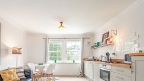 Moderni keittiö, jossa on valkoiset kaapit, kaasuliesi ja mikroaaltouuni. Keittiössä on ruokailutila, jossa on valkoinen pöytä ja tuolit, ja seinällä on suuri abstrakti maalaus.