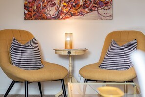 Two armchairs with patterned cushions, a small wooden table with a lamp, and a colorful abstract painting on the wall. - Abbey Street (No 8) (St Andrews)