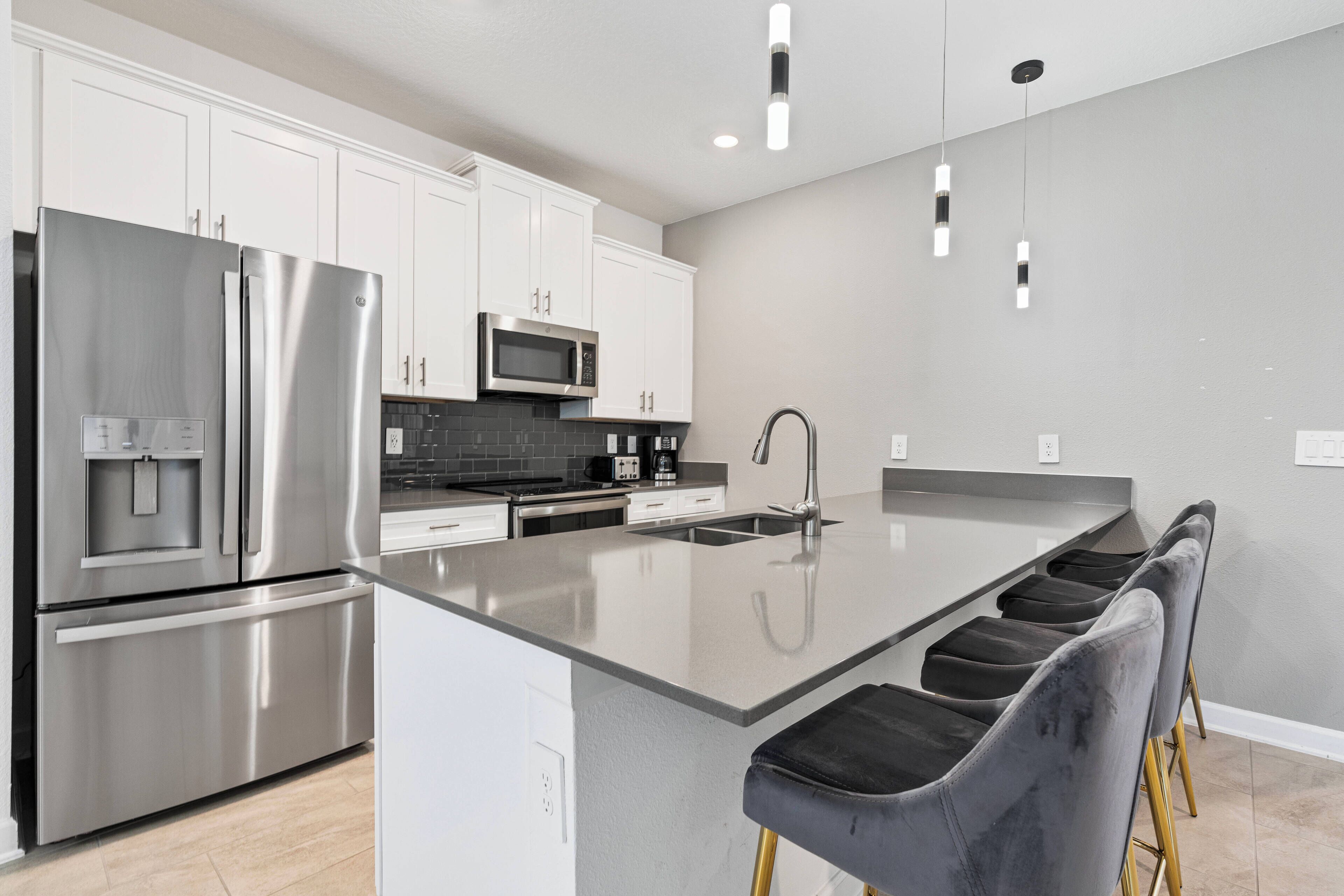 Una cocina moderna con electrodomésticos de acero inoxidable, armarios blancos y una isla central con taburetes de bar.