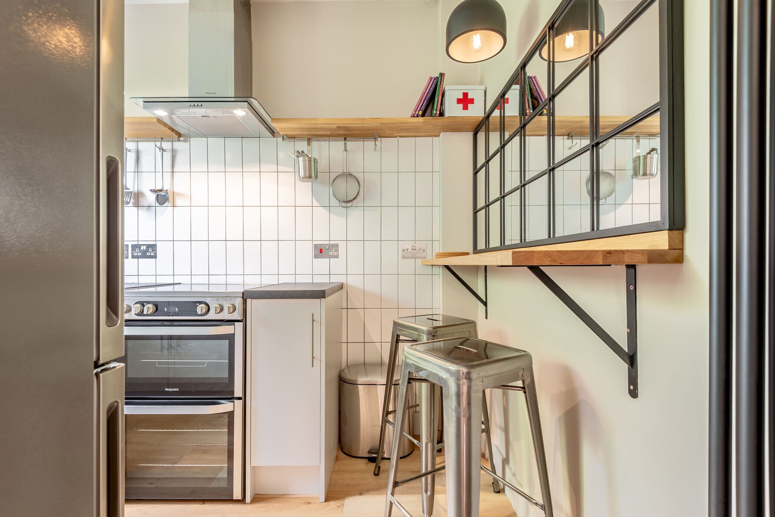 A kitchen with a built-in oven, a trash bin, and a stool.