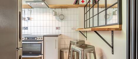 A kitchen with a built-in oven, a trash bin, and a stool.