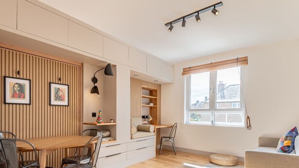 A modern room with a wooden slat wall, a dining area, a seating area with a sofa and a chair, and a window with a view. - Boase Avenue (No 69) | St Andrews (St Andrews)